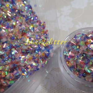 May include: A close-up of iridescent glitter in a clear plastic container. The glitter is a mix of pink, blue, and green colors. The glitter is in a small container and a larger container. The text "Made2glitter" is visible on the larger container.