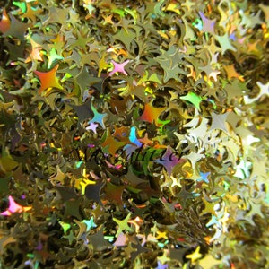 May include: A close-up image of iridescent gold glitter in the shape of stars. The glitter is scattered randomly and creates a shimmering effect.