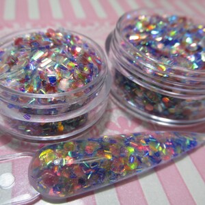 May include: Two small jars filled with iridescent glitter in shades of blue, pink, and green. A clear plastic spatula is filled with the same glitter.