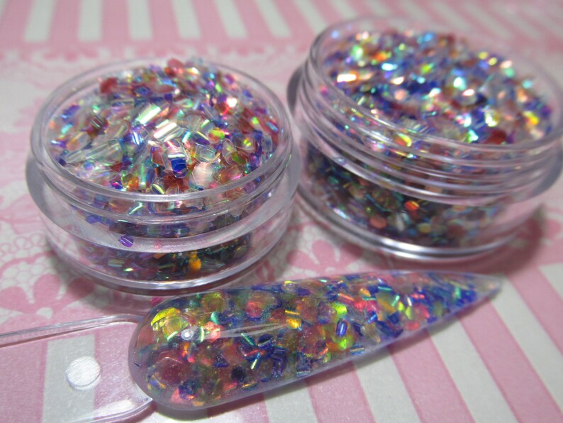 May include: Two small jars filled with iridescent glitter in shades of blue, pink, and green. A clear plastic spatula is filled with the same glitter.