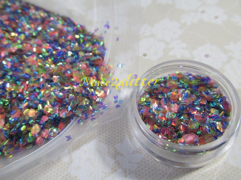 May include: A close-up of iridescent glitter in a clear plastic bag and a small clear jar. The glitter is a mix of pink, blue, green, and gold.