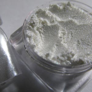May include: A small clear jar filled with a white iridescent glitter. The glitter is very fine and has a pearlescent sheen.