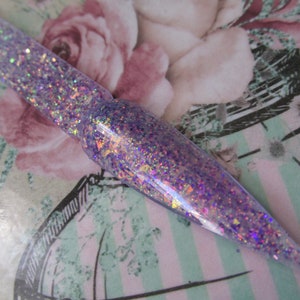May include: A close-up of a clear nail polish with iridescent purple and pink glitter.