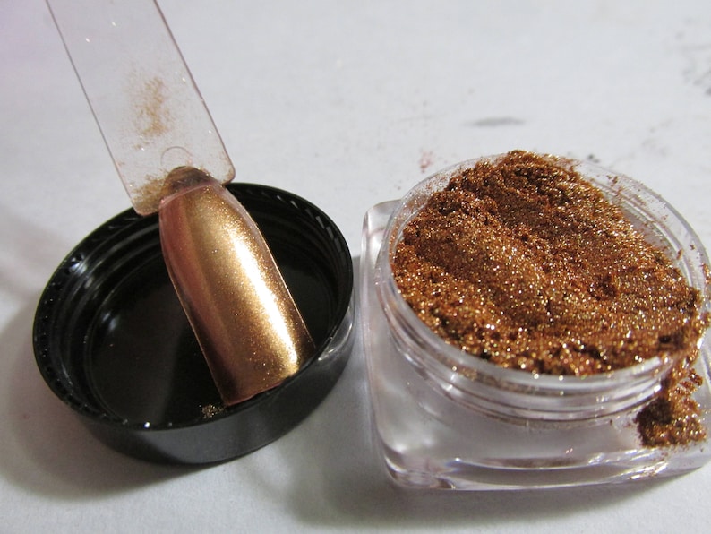 May include: A small jar of copper glitter with a clear lid. A clear plastic stick with a copper glitter coating is next to the jar.