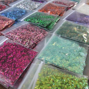 May include: Assortment of small bags filled with iridescent glitter in various colours, including green, pink, blue, and red.