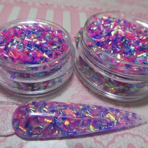 May include: Two small jars filled with iridescent pink and blue glitter flakes. A clear nail polish brush is coated with the glitter.