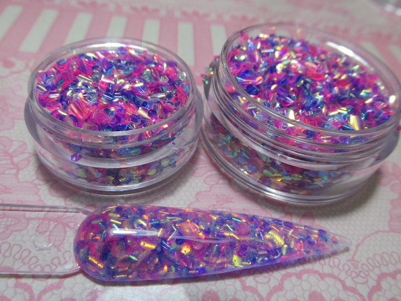 May include: Two small jars filled with iridescent pink and blue glitter flakes. A clear nail polish brush is coated with the glitter.