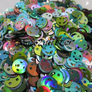 Op de afbeelding: Een close-up afbeelding van iriserende groene, blauwe en paarse glitter in de vorm van smiley's. De glitter is perfect voor knutselen en het toevoegen van glitter aan projecten.