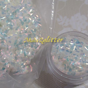 May include: A close-up of iridescent white glitter in a clear plastic bag and a clear jar. The glitter is small and has a holographic finish. The text "Made2glitter" is visible on the bag.