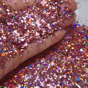 May include: A collection of loose, multi-sized hexagonal glitter particles in shades of copper, bronze, and rose gold. The glitter features a reflective, holographic finish that catches the light, creating vibrant flashes of blue, orange, and purple.