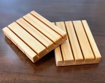 May include: Two wooden soap dishes with grooved surfaces. The dishes are made of light brown wood and are stacked on top of each other.