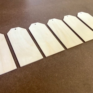 May include: Seven unfinished wooden tags with a hole punched in the top. The tags are arranged in a row from largest to smallest.