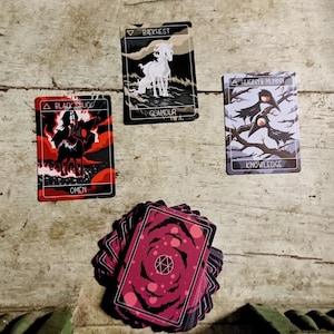 May include: A spread of tarot cards on a wooden surface. The cards show images of a black hooded figure, a white horse, and two black birds. The cards are labeled "Black Shroud", "Breach", "Lighter Fury", and "Knowledge".