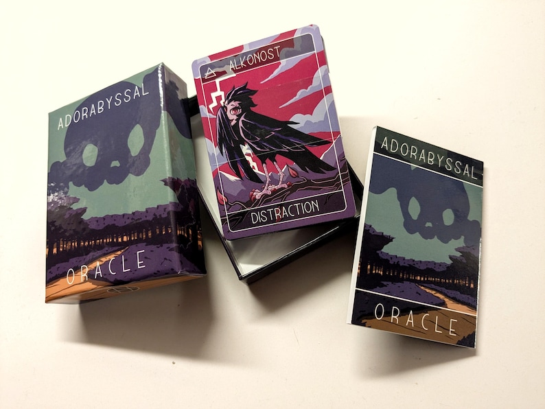 May include: A box of Adorabyssal Oracle cards with a single card pulled out. The card is red, pink, and blue with a black bird illustration and the text "ALKONOST DISTRACTION".