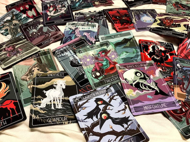 May include: A set of playing cards with colorful illustrations and text. The cards feature a variety of characters and creatures, including a white unicorn, a black bird, a skull, and a green elf. The cards are designed in a whimsical style with a dark background.