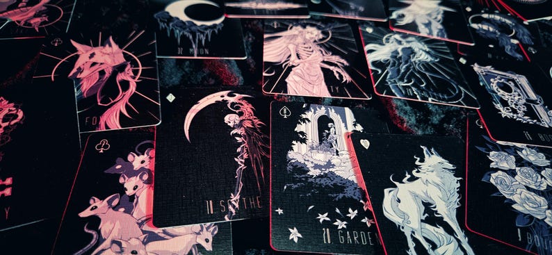 May include: A collection of tarot cards with dark backgrounds and illustrations in shades of pink, white, and blue. The cards feature images of animals, figures, and celestial bodies. The cards have red edges.