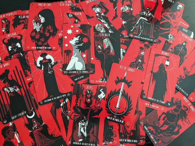 May include: A close-up of a spread of tarot cards with red backgrounds and black illustrations. The cards include the Emperor, Strength, Devil, Ace of Swords, Knight of Wands, and more.