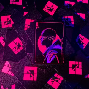 K&ouml;nnte beinhalten: Schwarze Spielkarten mit einem neonrosa geometrischen Design und einer zentralen Karte mit dem Profil einer Person mit futuristischen technischen Details. Die Karte tr&auml;gt den Text "YR PERSON". Der Hintergrund ist dunkel.