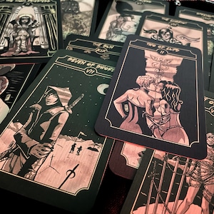May include: A collection of tarot cards with black backgrounds and illustrations in shades of red and gold. The cards feature various figures and symbols, including a hooded figure with a sword, and a couple kissing. The cards are spread out on a dark surface.