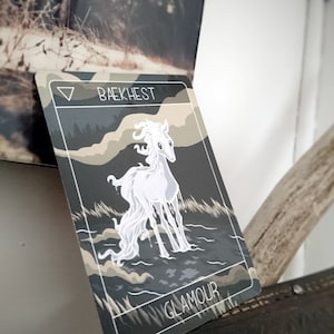 May include: A white horse with a flowing mane stands in a dark, misty forest. The card is titled "Baekhest" and "Glamour" in white text.