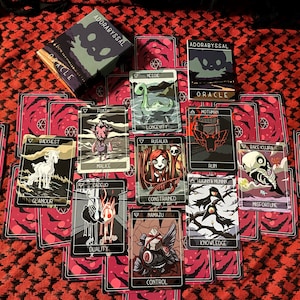 May include: A set of tarot cards with black and white illustrations of various creatures and characters. The cards have a red and black background with a white border. The cards are laid out in a spread on a red and black patterned surface. The box for the cards is green with a skull and the words "ADORABYSSAL ORACLE".