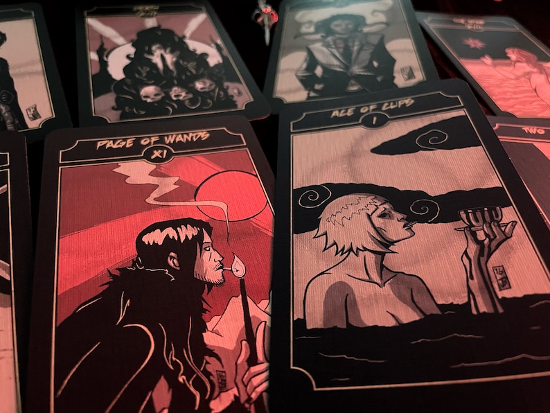 May include: A collection of tarot cards with black borders and illustrations in shades of gray and red. The "Page of Wands" card shows a figure with a lit match. The "Ace of Cups" card depicts a person in water. Other cards are visible.
