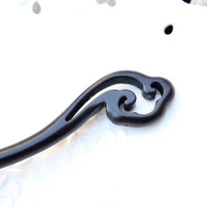 Pu&ograve; includere: Un fermacapelli in legno nero con un design a forma di nuvola nella parte superiore. L'accessorio per capelli &egrave; curvo e ha una finitura liscia e lucida. L'elemento decorativo presenta motivi a vortice e un design ritagliato.