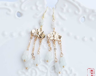 May include: A pair of gold earrings with white jade beads and a lotus flower design. The earrings are dangling and have a delicate chain.