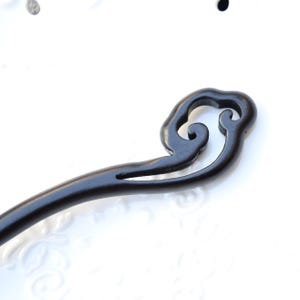 Pu&ograve; includere: Un fermacapelli in legno nero con un design decorativo a forma di nuvola. L'accessorio per capelli &egrave; scolpito con linee e curve morbide, progettato per tenere i capelli in posizione. Un accessorio per capelli tradizionale.