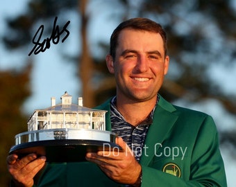 Puede incluir: Un hombre con una chaqueta verde sostiene un trofeo plateado con un pequeño edificio blanco en la parte superior. El trofeo está sobre una base negra. El hombre sonríe y tiene un parche verde en su chaqueta con una bola de golf blanca y un árbol verde. La firma "Sabas" está escrita con tinta negra en la esquina superior izquierda de la imagen.