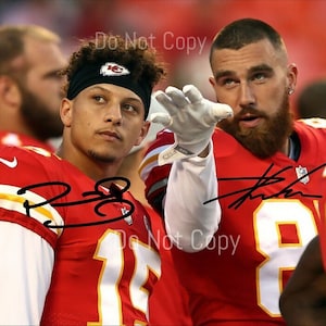 May include: Two football players in red and white jerseys. One player wears a black headband with a team logo. Both players have autographs on their jerseys. The image is a close-up of the players.