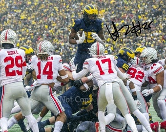 May include: A football player in a blue and yellow uniform jumps in the air to catch a football.  He is surrounded by players in white uniforms. The football player's jersey has the number 25 on it. The text "W25" is written in black ink on the image.