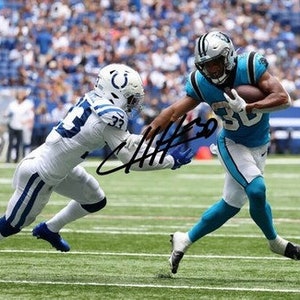 May include: A football player in a blue and white uniform runs with the ball while being tackled by a player in a white and blue uniform. The player in blue has the number 30 on his jersey.