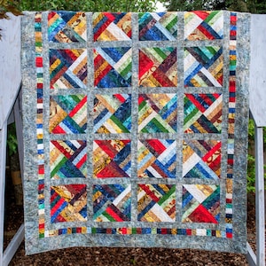 May include: A vibrant patchwork quilt with a geometric design. The quilt displays squares with diagonal stripes in shades of red, blue, green, and yellow. It has a grey mottled border.