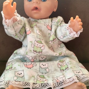 May include: A baby doll wearing a green and white owl print nightgown with white lace trim. The doll has blue eyes and a light pink complexion.