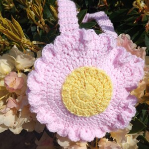 May include: A pink crocheted flower with a yellow center. The flower has a ruffled edge and is made with a soft yarn.