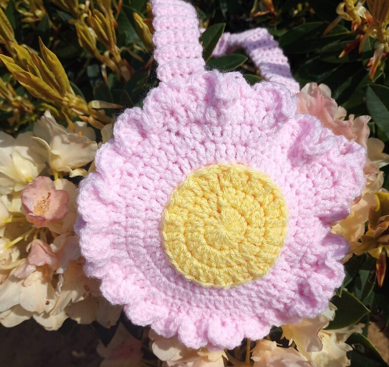 May include: A pink crocheted flower with a yellow center. The flower has a ruffled edge and is made with a soft yarn.