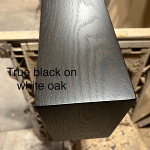 May include: Close-up of a rectangular piece of wood with a true black finish on white oak. The wood grain is visible. The text "True black on white oak" is printed on the wood.
