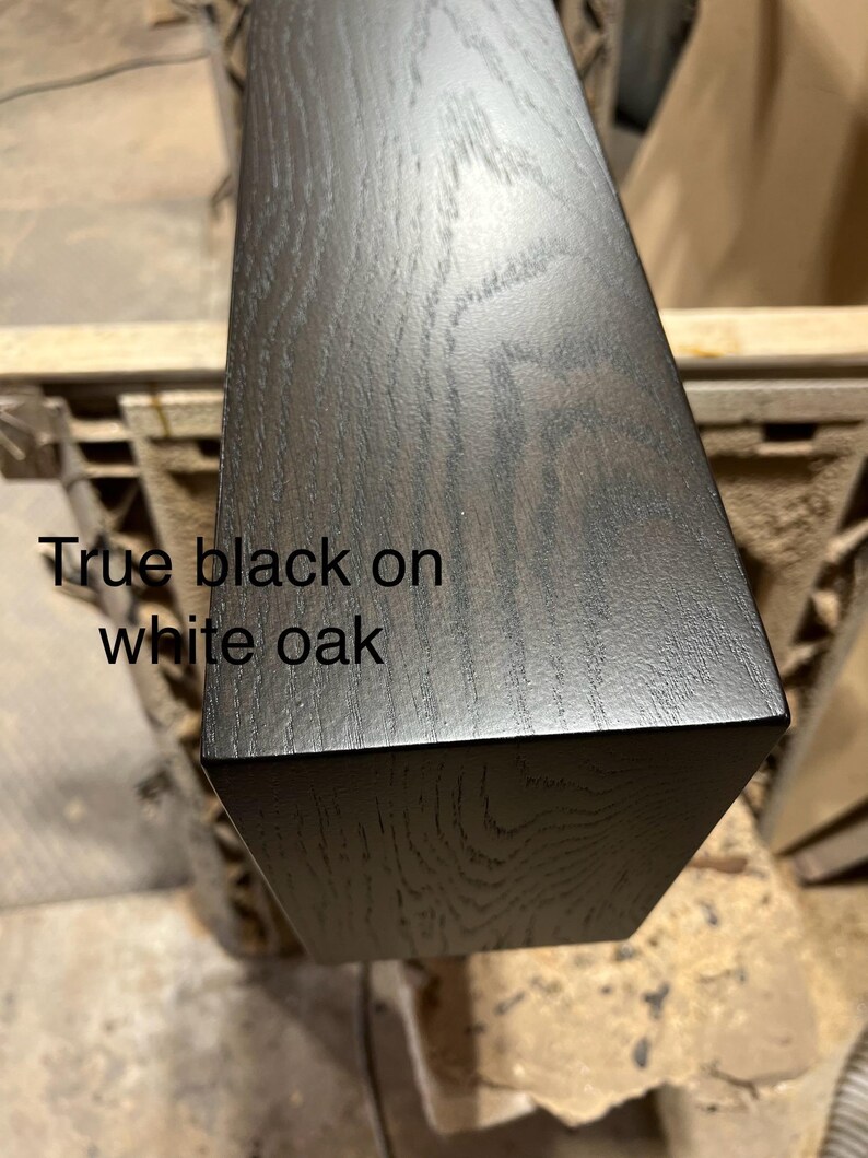 May include: Close-up of a rectangular piece of wood with a true black finish on white oak. The wood grain is visible. The text "True black on white oak" is printed on the wood.