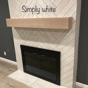 May include: A fireplace with a light wood mantel and a black framed firebox. The surround is tiled in a white herringbone pattern. The text "Simply white" is written across the top of the fireplace.