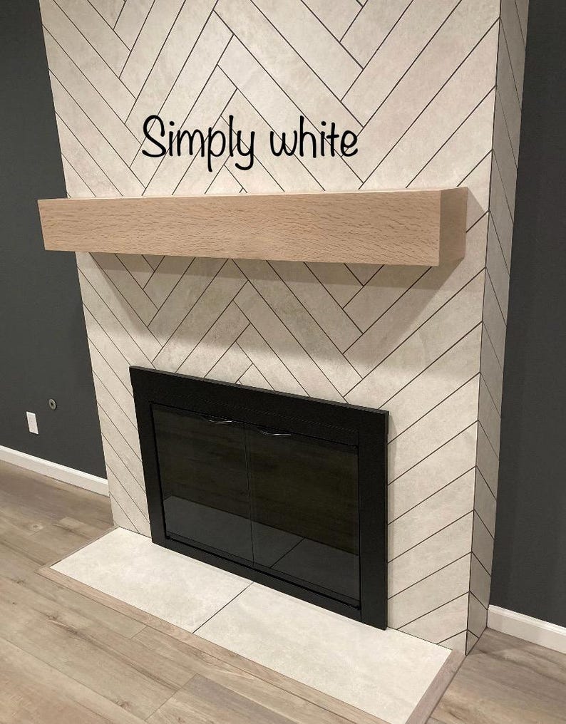 May include: A fireplace with a light wood mantel and a black framed firebox. The surround is tiled in a white herringbone pattern. The text "Simply white" is written across the top of the fireplace.
