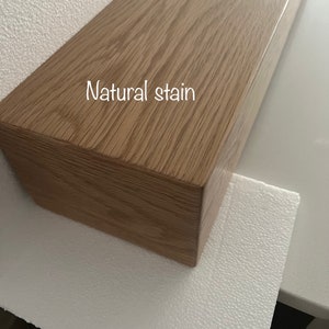 May include: A rectangular wooden shelf with a natural stain finish. The wood grain is visible, and the text "Natural stain" is printed on the surface. The shelf is light brown and appears to be new.