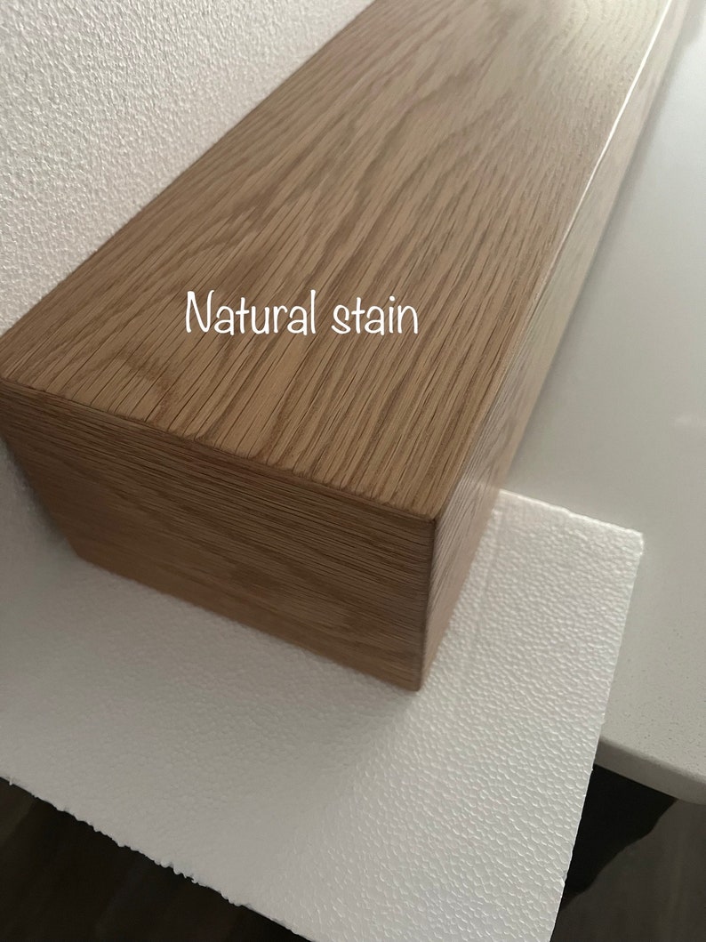 May include: A rectangular wooden shelf with a natural stain finish. The wood grain is visible, and the text "Natural stain" is printed on the surface. The shelf is light brown and appears to be new.