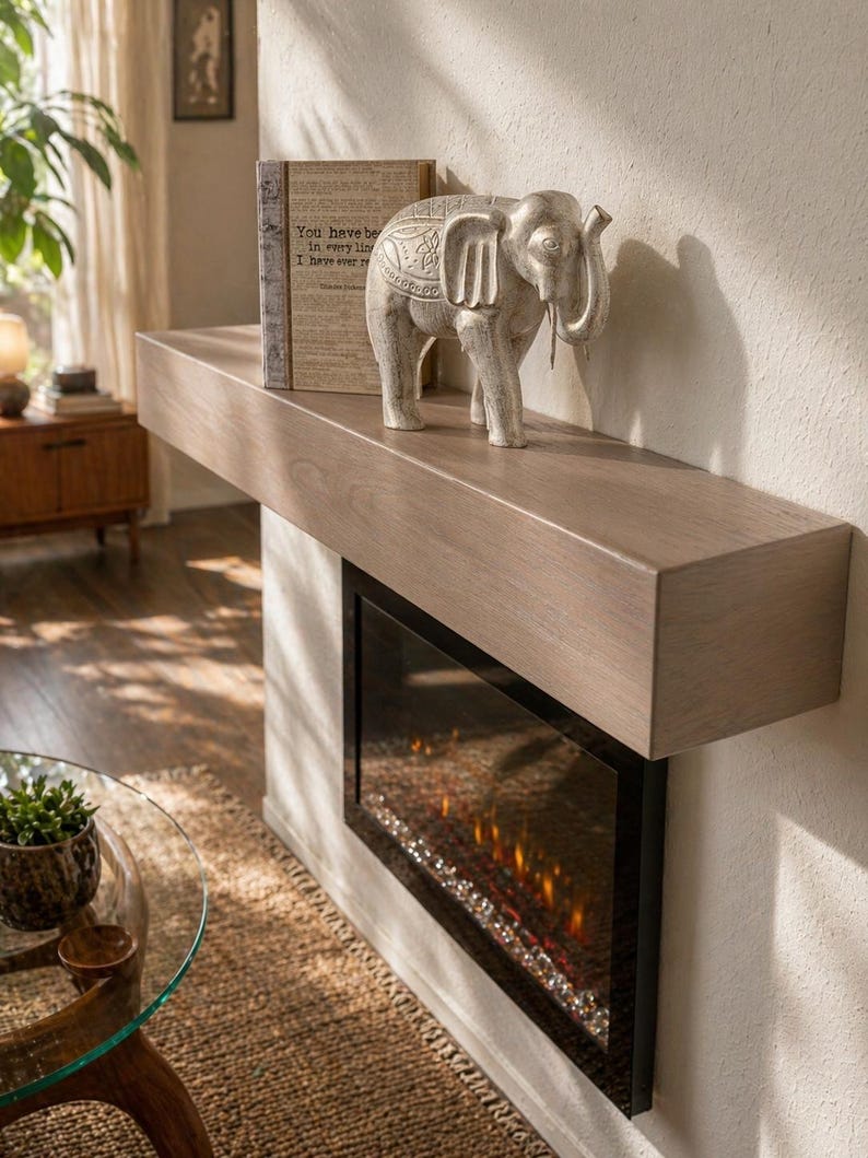 May include: A gray wooden mantel with a built-in electric fireplace. A decorative elephant statue and a book with text are on the mantel. The fireplace has a black frame and a glowing ember effect.