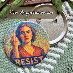 Op de afbeelding: Een ronde button met een neo-impressionistisch ontwerp. De button toont een portret van een persoon met de middelvinger omhoog, met het woord "RESIST" in blauw en geel. De achtergrond is een kleurrijk moza&iuml;ek.