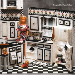 May include: A plastic canvas dollhouse kitchen set with black and white checkered flooring. The kitchen features a white refrigerator with a black handle, a white oven with a black handle, a white sink with a black faucet, and a white countertop with black trim. The kitchen also includes a doll, a cat, and a dog.