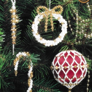 Puede incluir: Cuatro adornos navideños de cuentas colgando de un árbol de Navidad verde. Los adornos son una caña de azúcar de cuentas blancas, una corona de cuentas blancas con un lazo dorado, una bola de cuentas blancas con un centro rojo y un carámbano de cuentas blancas.