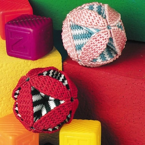 May include: A collection of colorful children's toys. The image features two knitted balls in red, pink, and blue, along with several plastic alphabet blocks in various colors. The blocks are orange, yellow, purple, and red.