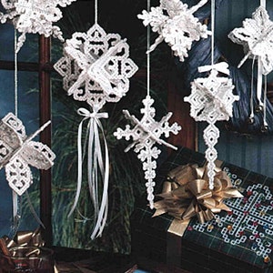 Puede incluir: Una colección de adornos de copo de nieve de ganchillo blanco que cuelgan de una cuerda blanca. Los adornos están decorados con lazos de cinta blanca. Los adornos cuelgan frente a un fondo verde oscuro y marrón.