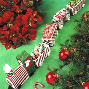 Puede incluir: Un tren de Navidad hecho de fieltro con rayas rojas y blancas y detalles verdes. El tren está lleno de bastones de caramelo y otras golosinas navideñas. El tren está sobre un fondo verde con poinsettias rojas y una guirnalda verde con adornos rojos.